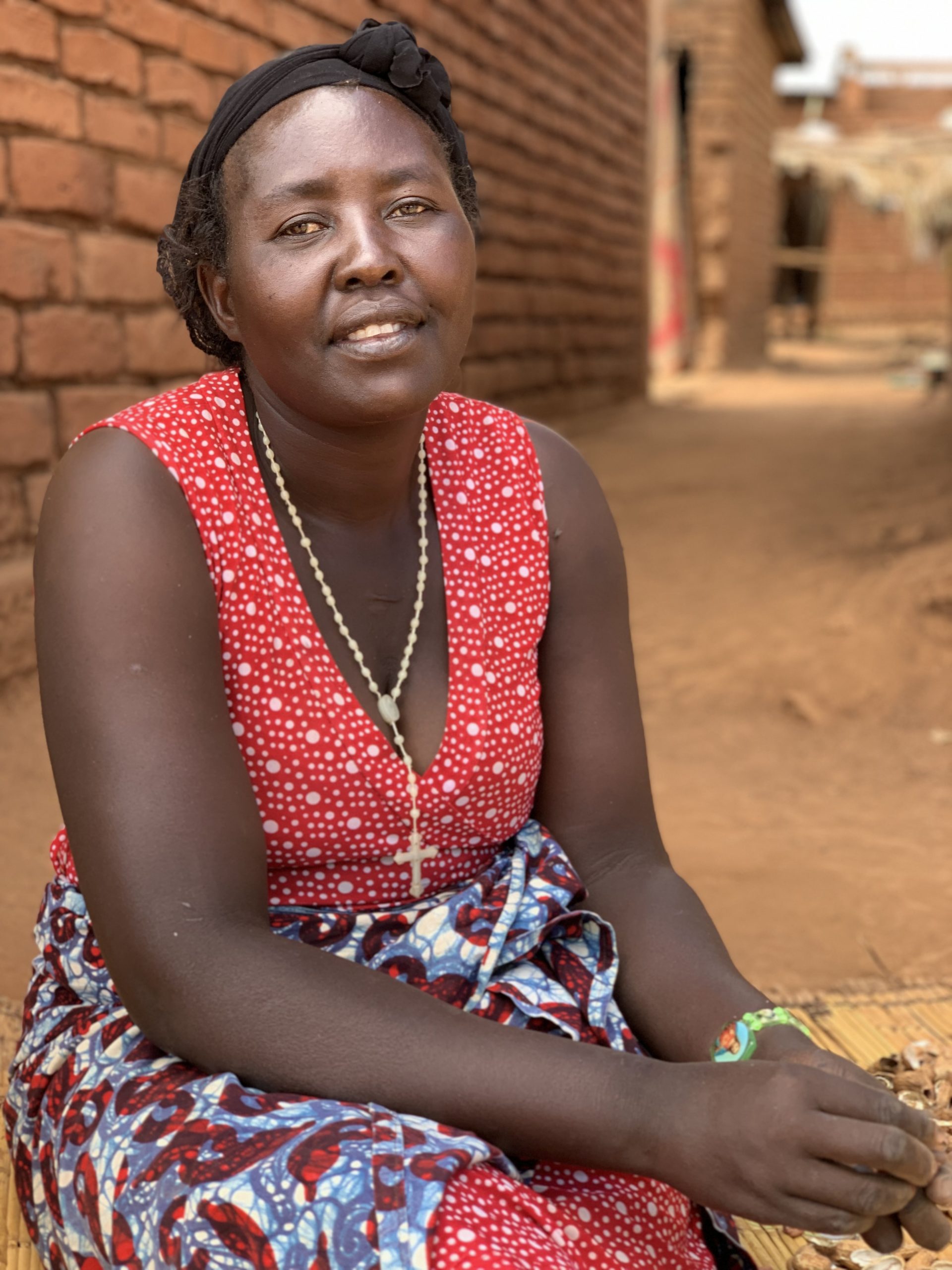 Anita Chitaya, an malwian woman sits in front of a clay brick house