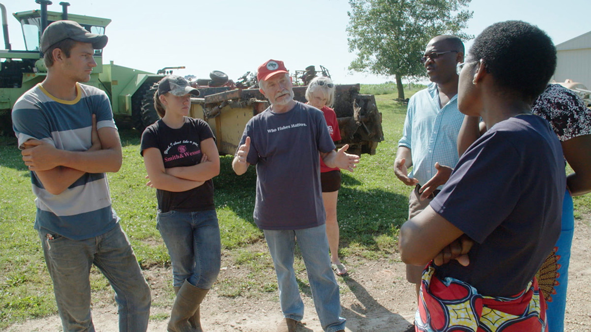4 american farm hand speaking with 3 african activists with large farming equipment in the backgroun